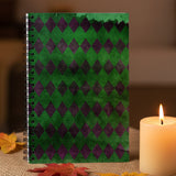 Notebook with green and purple diamond pattern next to a candle on a wooden surface.